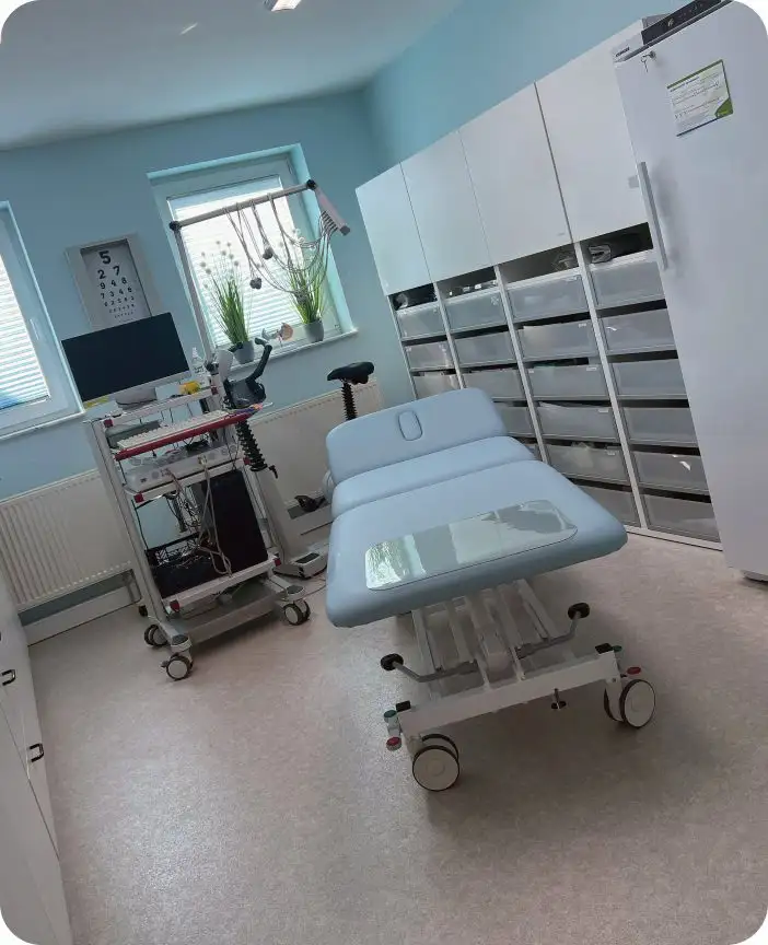 Dieses Bild zeigt einen professionell eingerichteten Untersuchungsraum in einer modernen Arztpraxis. Im Mittelpunkt steht eine komfortable Untersuchungsliege mit hellblauer Polsterung, die für Patienten bereitsteht. Die hellblauen Wände und das natürliche Licht durch das Fenster mit grünen Zimmerpflanzen schaffen eine beruhigende und hygienische Atmosphäre. Rechts im Bild befinden sich medizinische Schränke und Schubladen, die zur Aufbewahrung von Praxisbedarf und medizinischen Geräten dienen. Links ist ein mobiler Gerätekarren mit verschiedenen medizinischen Instrumenten zu sehen – ideal für flexible Anwendungen während der Untersuchung. Diese Praxis vereint funktionale Ausstattung mit patientenfreundlichem Design und eignet sich hervorragend für Allgemeinmedizin, Innere Medizin oder ambulante Behandlungen. Die klare Raumstruktur und das sterile Umfeld vermitteln Vertrauen und Professionalität, wie sie in einer zertifizierten medizinischen Einrichtung erwartet werden.